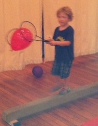 This camper has a lot going on! He walks across the balance beam without falling off, while delicately carrying a balloon between two rackets without popping or dropping it! What skill!